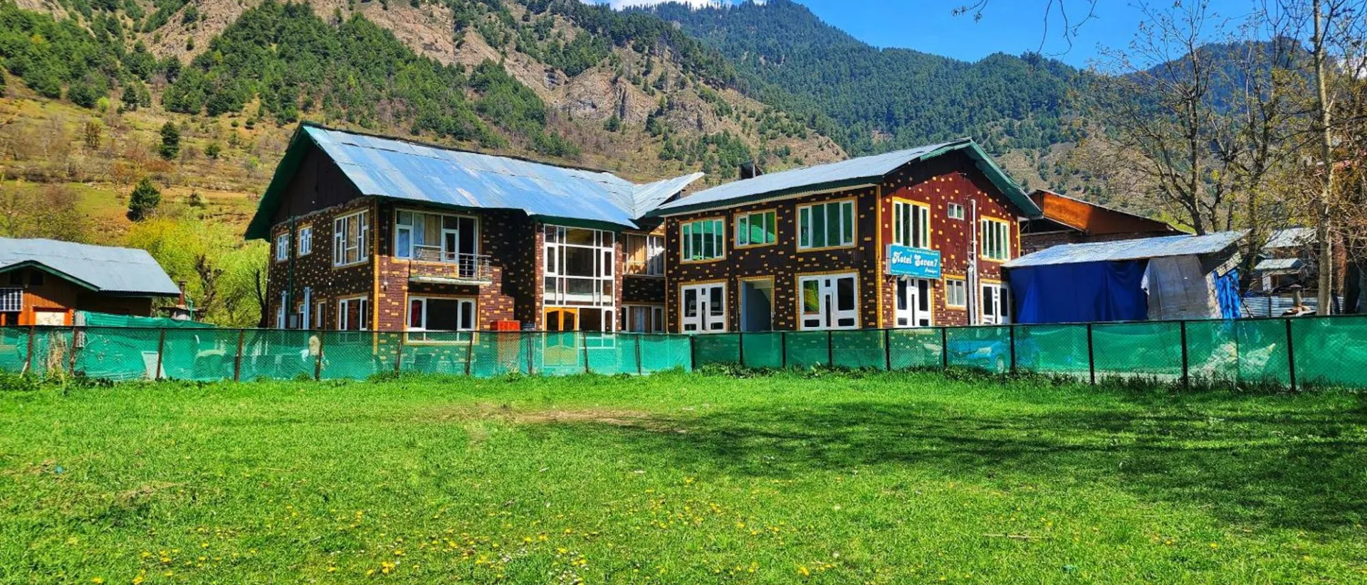 Exterior of Hotel Seven Pahalgam with its lawn and the hillside behind
